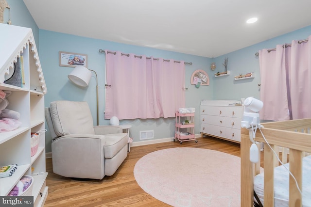 bedroom with a crib, recessed lighting, baseboards, wood finished floors, and visible vents