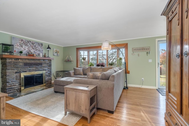 living area featuring a stone fireplace, ornamental molding, light wood-style flooring, and baseboards