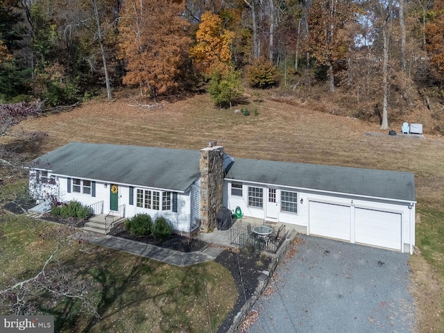 view of front facade with an attached garage, roof with shingles, driveway, and a chimney