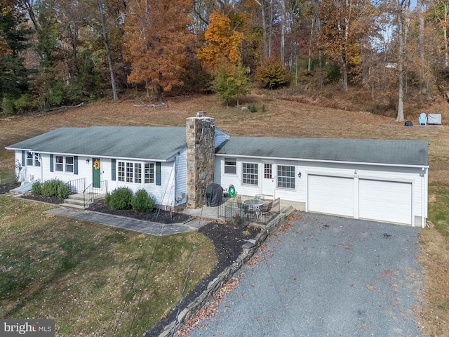 ranch-style home featuring a garage, a chimney, a shingled roof, and gravel driveway