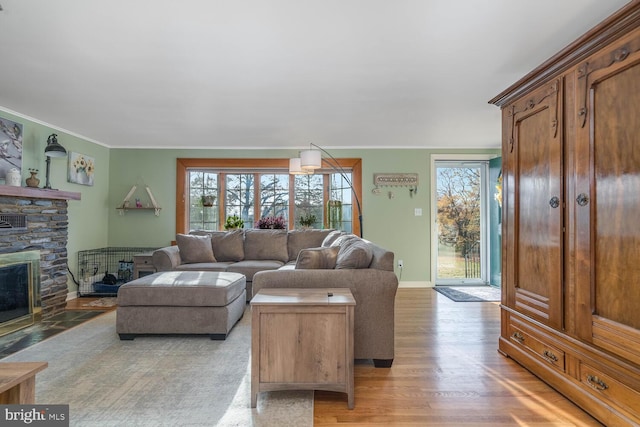living area with a healthy amount of sunlight, crown molding, light wood-type flooring, and a stone fireplace
