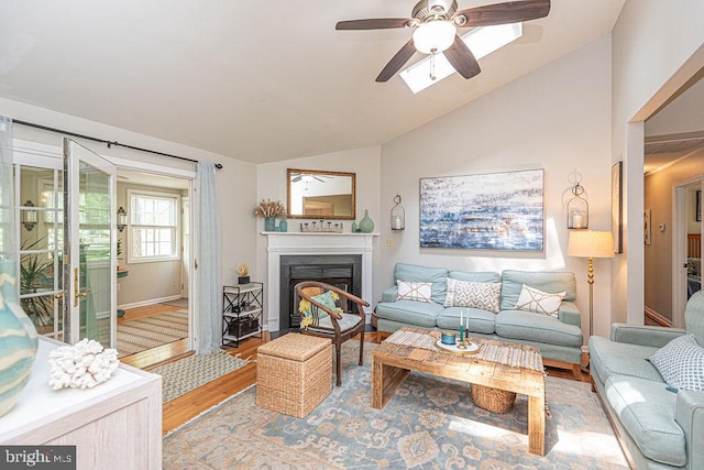 living area with a ceiling fan, a fireplace with flush hearth, vaulted ceiling, baseboards, and light wood finished floors
