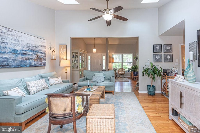 living room featuring a ceiling fan, a skylight, and high vaulted ceiling