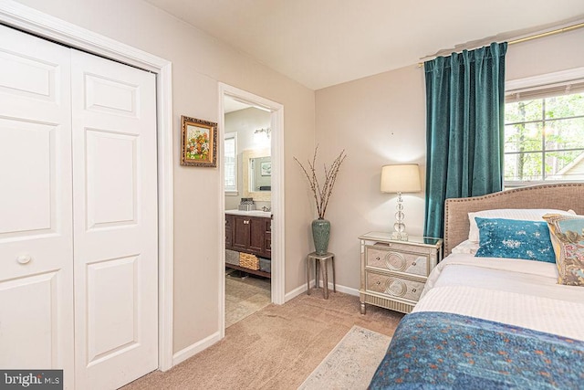 bedroom featuring baseboards, ensuite bathroom, a closet, and light carpet