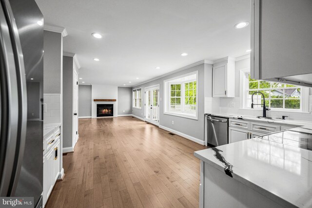 kitchen featuring stainless steel appliances, a warm lit fireplace, open floor plan, a sink, and baseboards