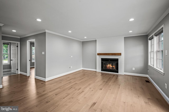 unfurnished living room featuring recessed lighting, wood finished floors, plenty of natural light, ornamental molding, and a glass covered fireplace