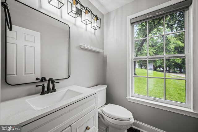 half bathroom with healthy amount of natural light, toilet, vanity, and baseboards
