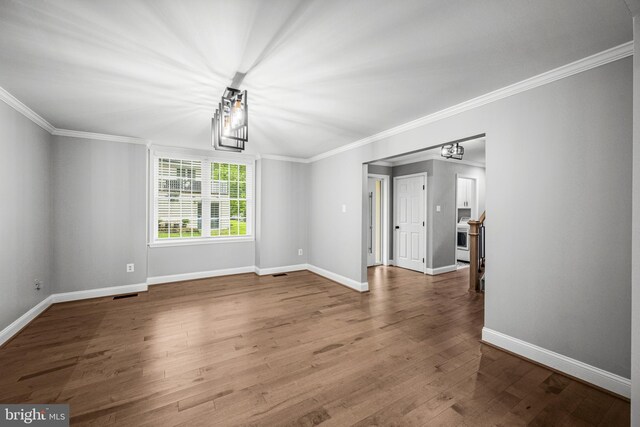 empty room featuring crown molding, baseboards, wood finished floors, and a chandelier