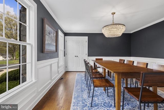 dining area featuring dark wood-style floors, a notable chandelier, ornamental molding, and a healthy amount of sunlight