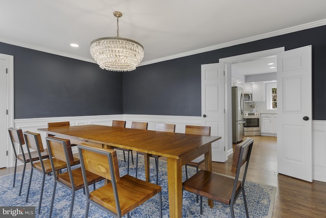 dining area featuring ornamental molding, wainscoting, wood finished floors, and a chandelier