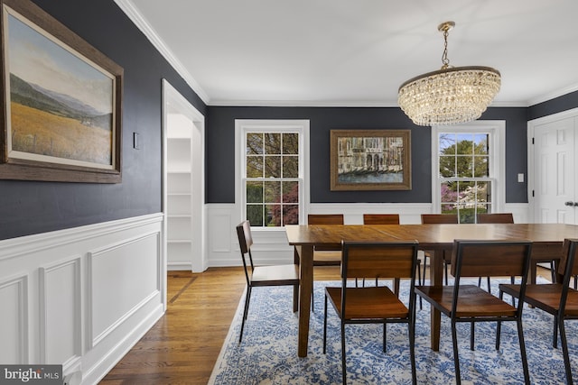 dining area featuring ornamental molding, wainscoting, a decorative wall, wood finished floors, and a chandelier