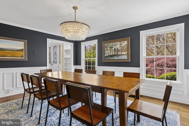 dining area featuring an inviting chandelier, ornamental molding, a decorative wall, a wainscoted wall, and dark wood finished floors