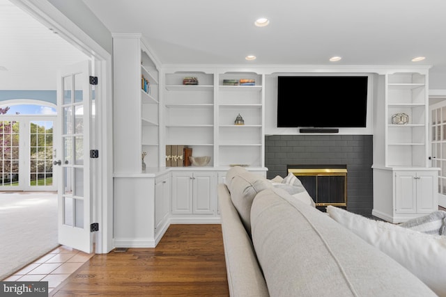 living room featuring a brick fireplace, recessed lighting, built in features, and wood finished floors