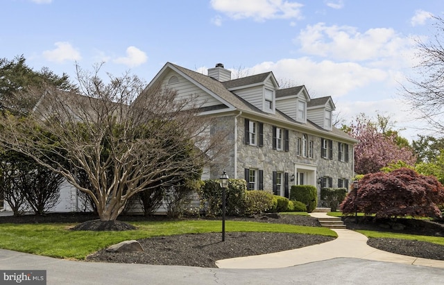 colonial-style house with a shingled roof, a chimney, and stone siding