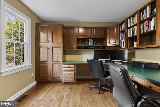 office area with plenty of natural light, light wood-style flooring, built in desk, and visible vents