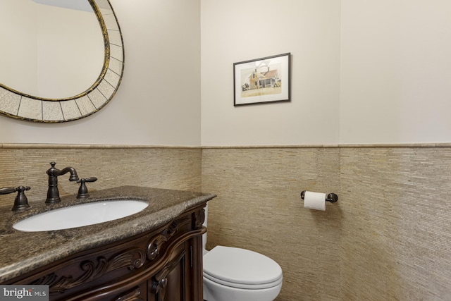 half bathroom with vanity, a wainscoted wall, toilet, and tile walls