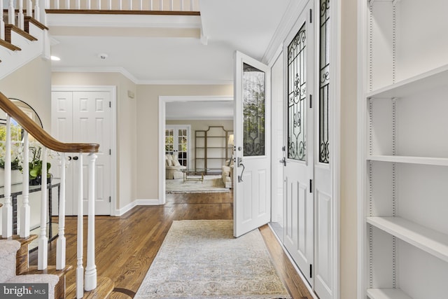 entryway featuring crown molding, baseboards, wood finished floors, and stairway
