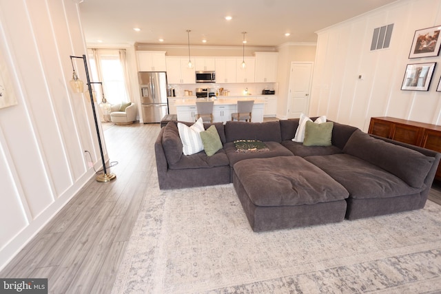 living area with light wood-style flooring, crown molding, recessed lighting, and a decorative wall