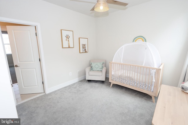 carpeted bedroom with a crib, baseboards, and ceiling fan
