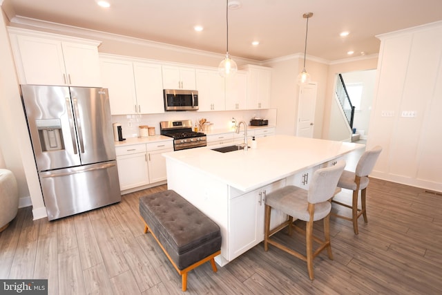 kitchen with stainless steel appliances, a sink, white cabinetry, decorative backsplash, and a kitchen island with sink
