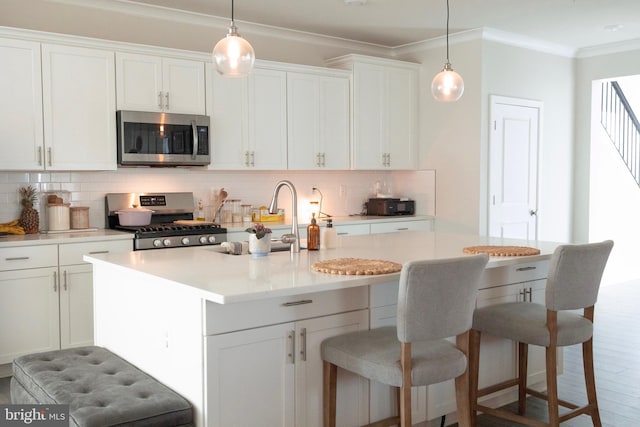 kitchen with stainless steel appliances, crown molding, a sink, backsplash, and an island with sink