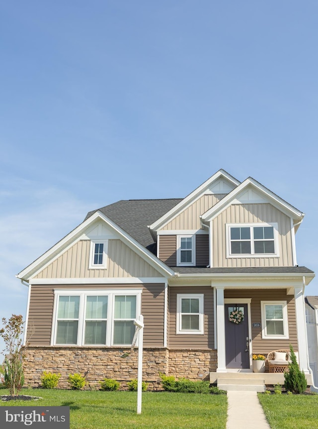 craftsman-style house with stone siding, board and batten siding, covered porch, and a front yard