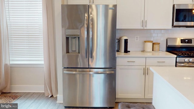 kitchen with stainless steel appliances, white cabinets, tasteful backsplash, light countertops, and light wood-type flooring