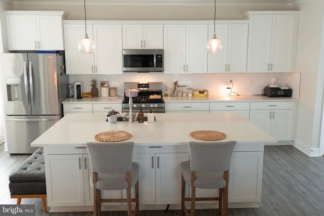 kitchen featuring appliances with stainless steel finishes, white cabinets, a kitchen breakfast bar, tasteful backsplash, and decorative light fixtures