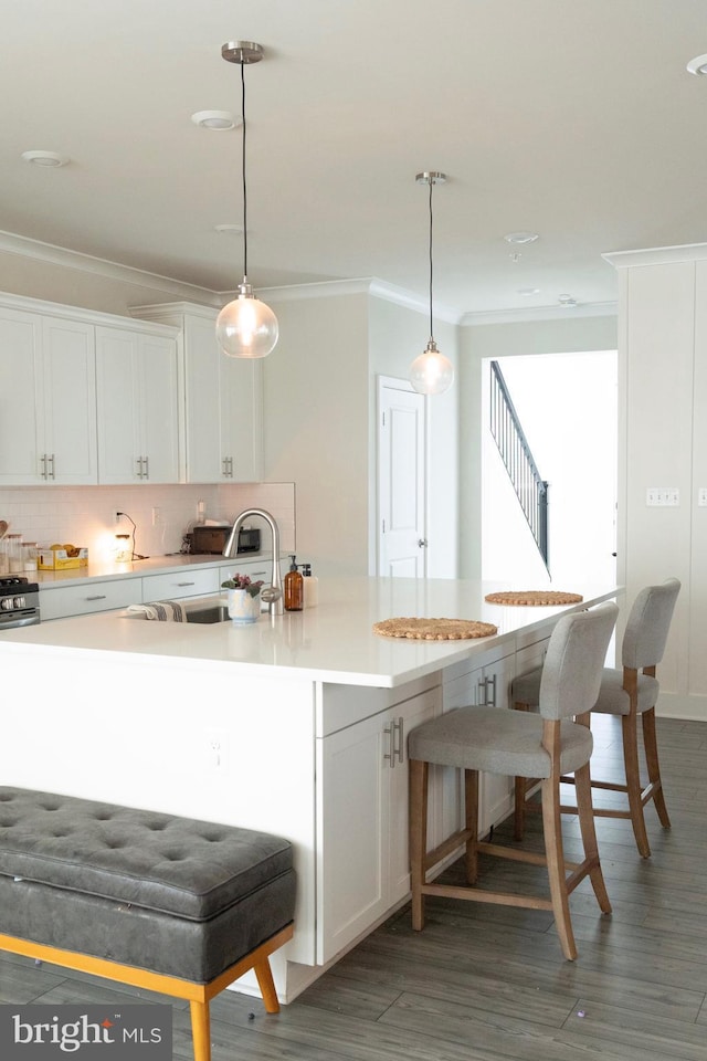 kitchen with crown molding, backsplash, white cabinets, a breakfast bar area, and light countertops