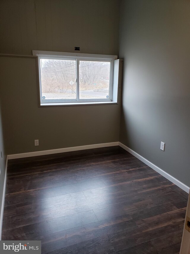 unfurnished room featuring baseboards and dark wood finished floors