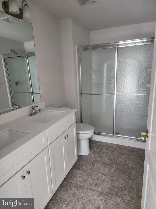 bathroom featuring a stall shower, toilet, and double vanity