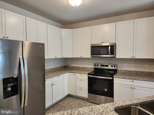 kitchen with stainless steel appliances, white cabinetry, and light stone counters