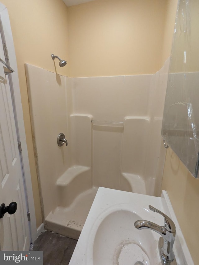full bathroom featuring a sink, a shower, and wood finished floors