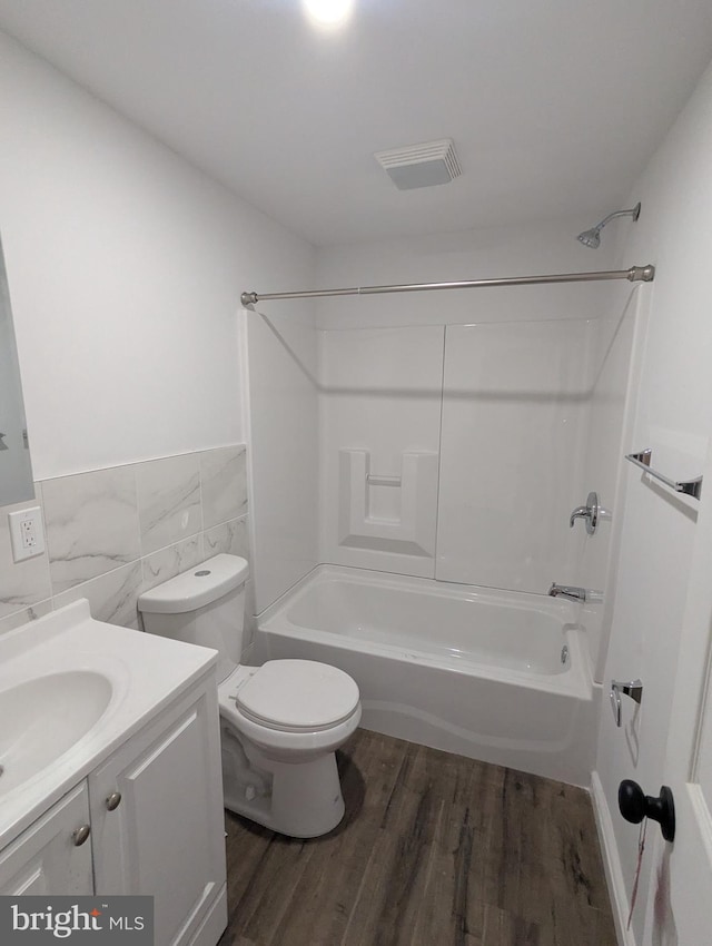 full bathroom with visible vents, vanity, wood finished floors, tile walls, and shower / washtub combination