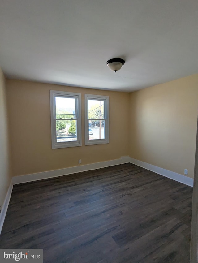 spare room with baseboards and dark wood-type flooring