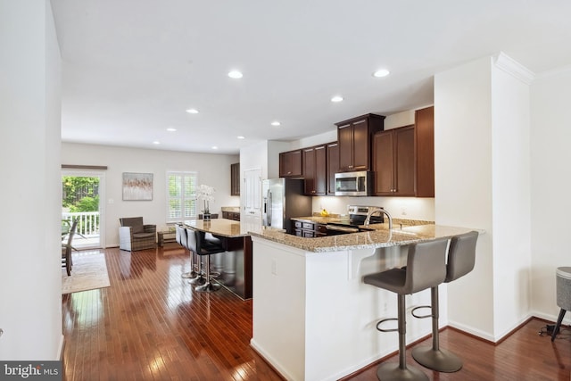 kitchen featuring light stone countertops, appliances with stainless steel finishes, dark brown cabinetry, a kitchen breakfast bar, and dark wood-type flooring