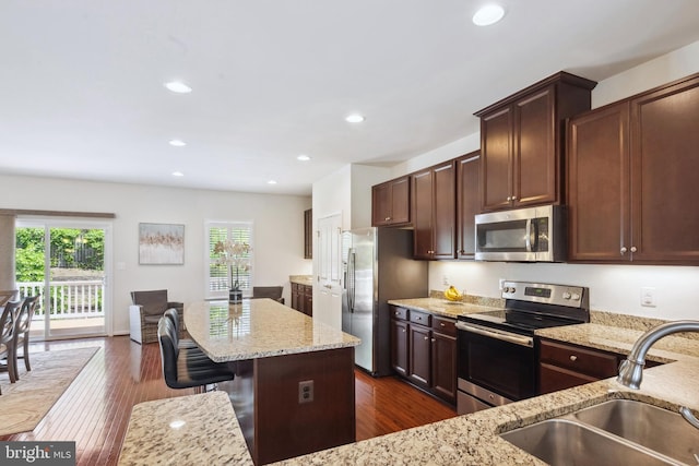 kitchen with appliances with stainless steel finishes, light stone counters, a sink, a breakfast bar area, and dark wood finished floors