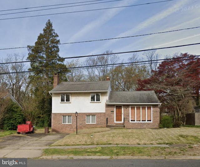 split level home featuring a chimney, a front yard, driveway, and brick siding