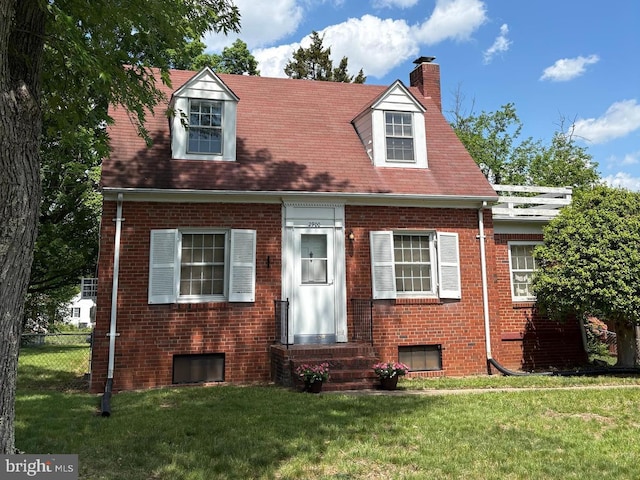 new england style home featuring fence, a chimney, a front yard, and brick siding
