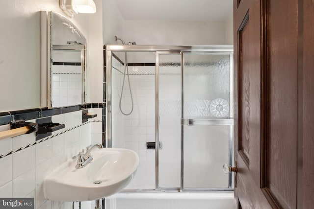 bathroom with tile walls, enclosed tub / shower combo, and a sink