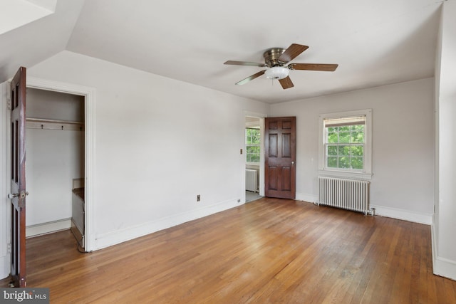 unfurnished bedroom featuring radiator, baseboards, light wood finished floors, and ceiling fan