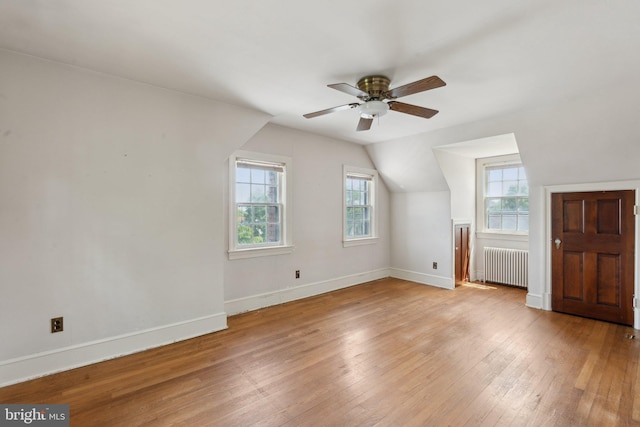 additional living space featuring ceiling fan, baseboards, lofted ceiling, radiator heating unit, and light wood-style flooring