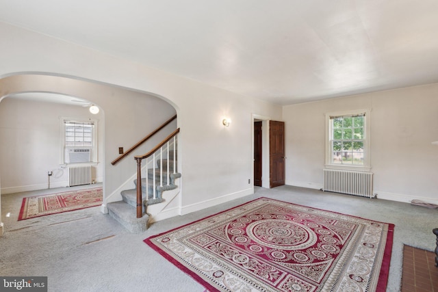 carpeted entrance foyer featuring baseboards, arched walkways, and radiator heating unit