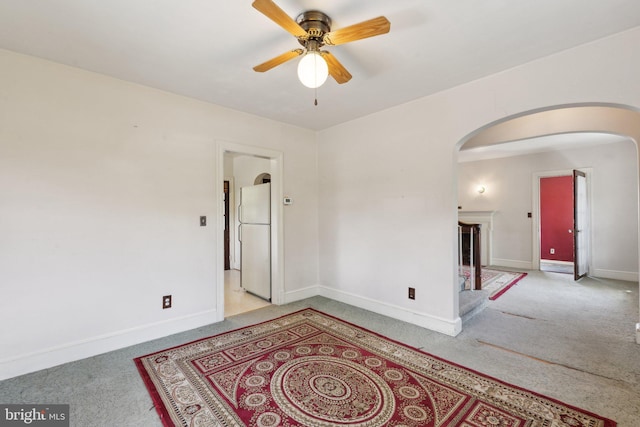 carpeted empty room featuring arched walkways, a ceiling fan, and baseboards