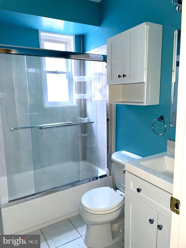 full bath with tile patterned flooring, bath / shower combo with glass door, toilet, and vanity