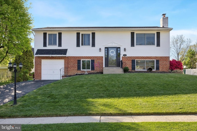 bi-level home with an attached garage, aphalt driveway, a front yard, and a chimney