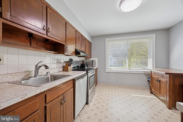 kitchen featuring appliances with stainless steel finishes, a sink, baseboards, tasteful backsplash, and under cabinet range hood