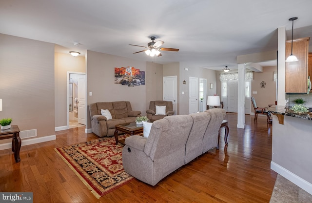 living room with a ceiling fan, visible vents, wood finished floors, baseboards, and ornate columns