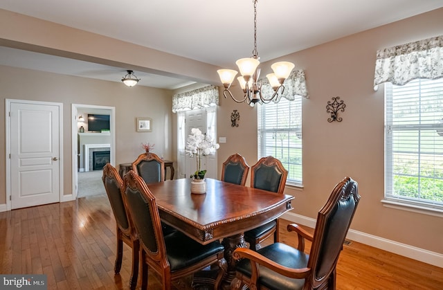 dining area featuring baseboards, light wood-style floors, a glass covered fireplace, and a chandelier