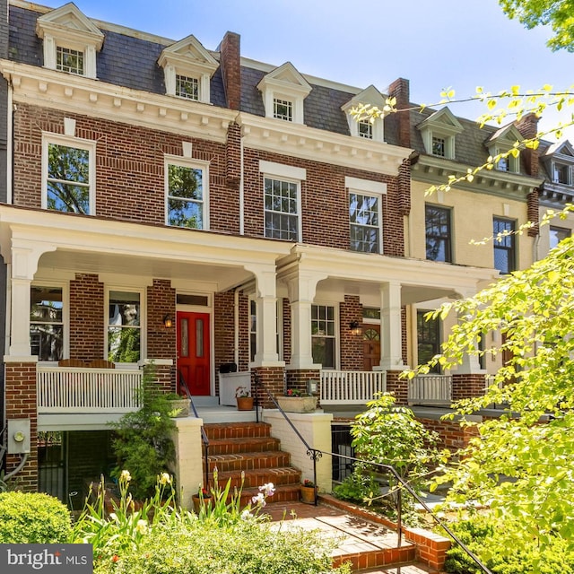 view of front of home featuring covered porch, brick siding, and mansard roof